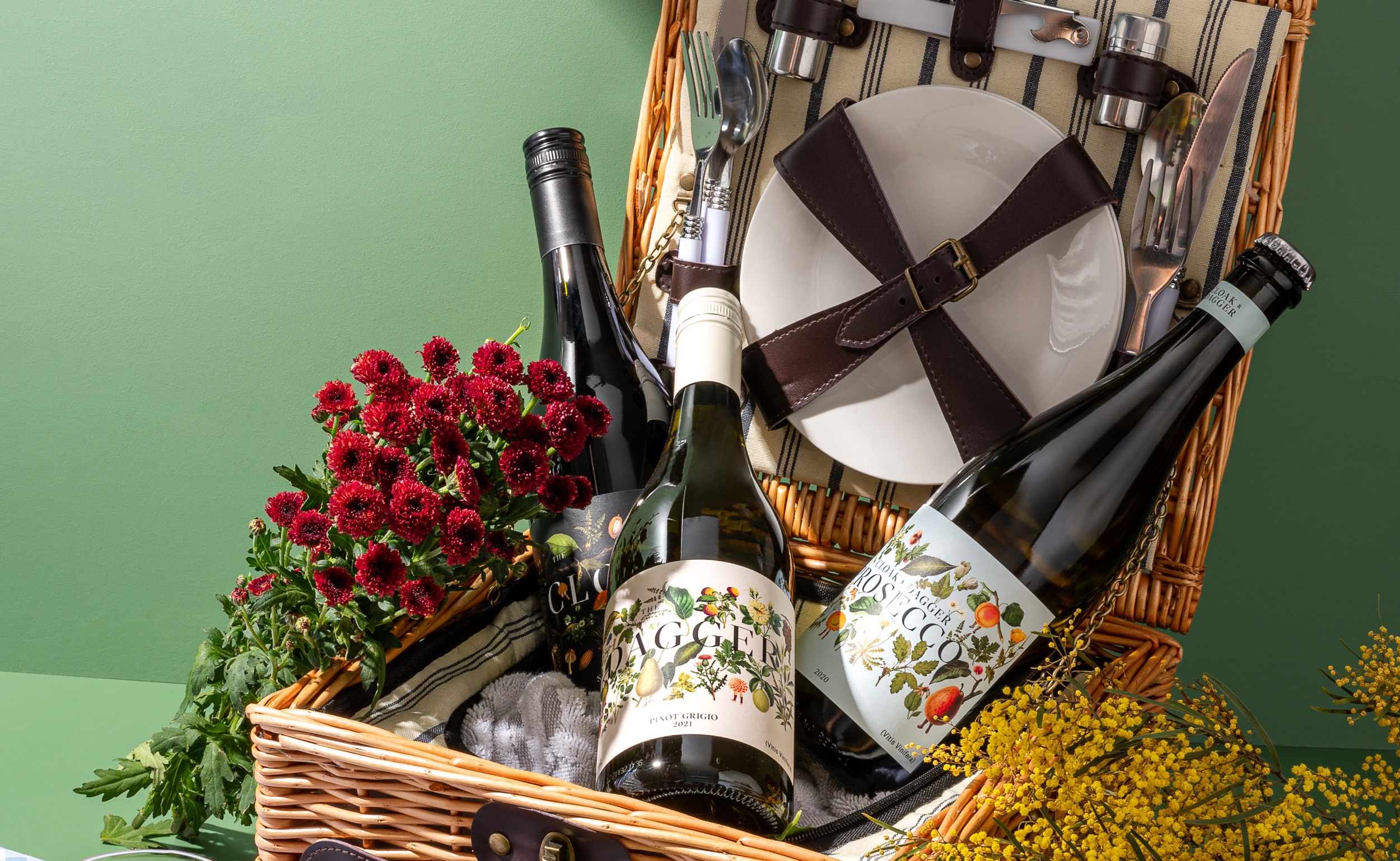 Three bottles of CLoak and Dagger wine in a picnic basket with flowers.